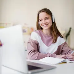 Uśmiechnięta dziewczyna w słuchawkach pisze w zeszycie, pracując nad swoim opinion essay.