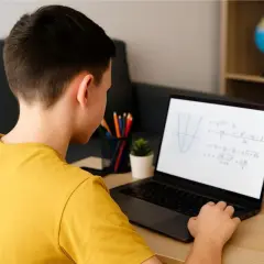 Chłopiec z pokolenia Alfa uczy się matematyki online. Na ekranie laptopa widać wykres funkcji i równania.