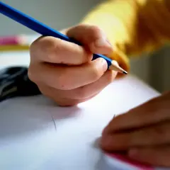 Dłoń podmiotu lirycznego trzyma niebieską kredkę, rysując na białej kartce. Obok leżą nożyczki.