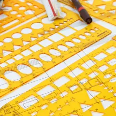 Żółte przyrządy kreślarskie, cyrkiel i linijka tworzą kompozycję do rysunku technicznego, gdzie wymiarowanie jest kluczowe.