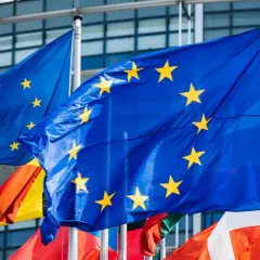 Flagi Unii Europejskiej powiewają przed nowoczesnym budynkiem, symbolizując jedność i współpracę krajów członkowskich.