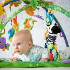 Niemowlę leży na macie edukacyjnej z zabawkami: żyrafą, zebrą i ptaszkiem.
