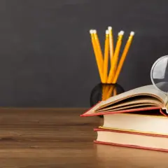 Stos książek, lupa i ołówki na biurku. Idealne do nauki lektury klasa 5.