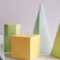 Różnokolorowe bryły geometryczne: żółty sześcian, zielony graniastosłup, dwa ostrosłupy prawidłowe (jasnoniebieski i żółty) oraz niebieski trójkąt.