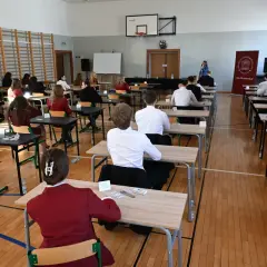 Uczniowie siedzą w ławkach, skupieni na pisaniu egzaminu. To ważny moment, przygotowanie do lektury na maturę.