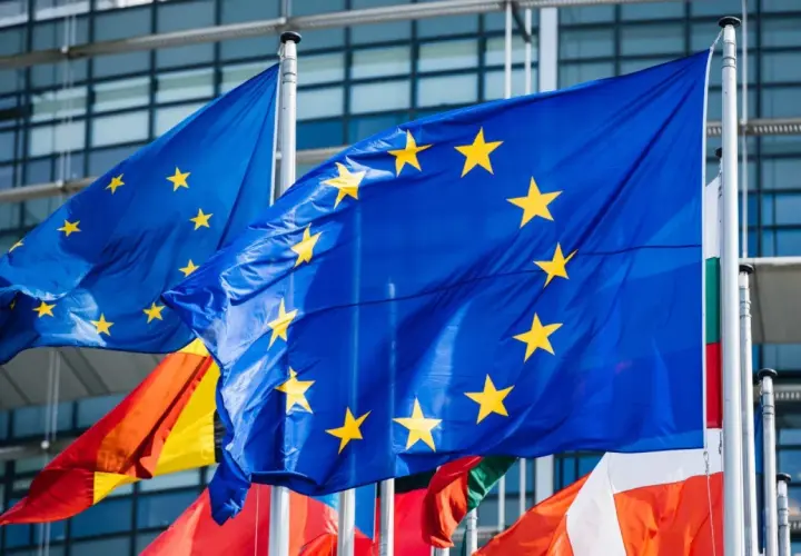 Flagi Unii Europejskiej powiewają przed nowoczesnym budynkiem, symbolizując jedność i współpracę krajów członkowskich.
