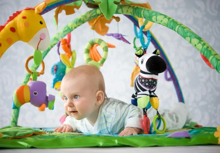 Niemowlę leży na macie edukacyjnej z zabawkami: żyrafą, zebrą i ptaszkiem.