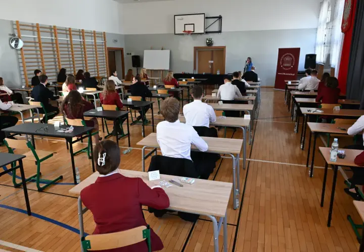 Uczniowie siedzą w ławkach, skupieni na pisaniu egzaminu. To ważny moment, przygotowanie do lektury na maturę.