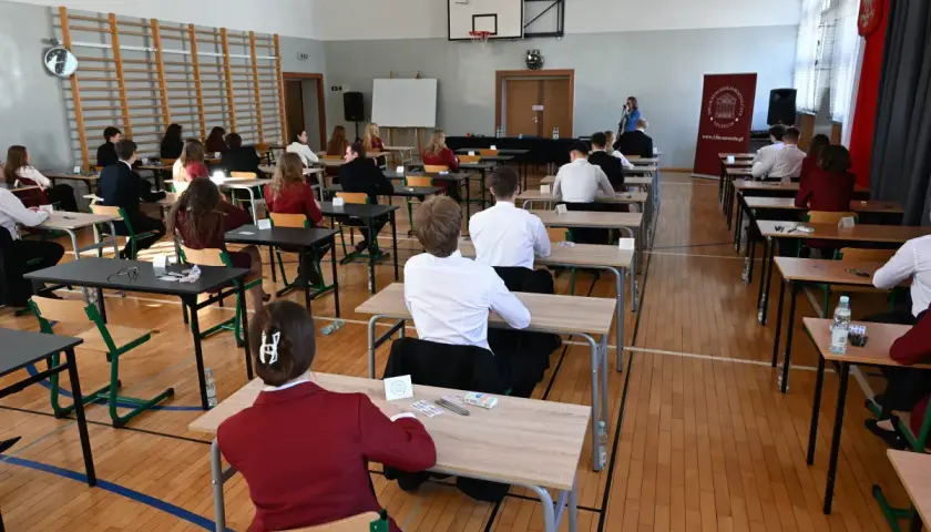 Uczniowie siedzą w ławkach, skupieni na pisaniu egzaminu. To ważny moment, przygotowanie do lektury na maturę.