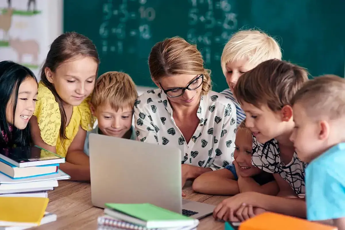 Nauczycielka z uczniami przy laptopie. Szukają informacji, gdzie znaleźć sprawdziany z nowej ery.