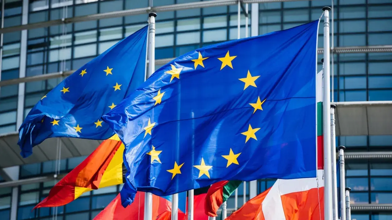 Flagi Unii Europejskiej powiewają przed nowoczesnym budynkiem, symbolizując jedność i współpracę krajów członkowskich.
