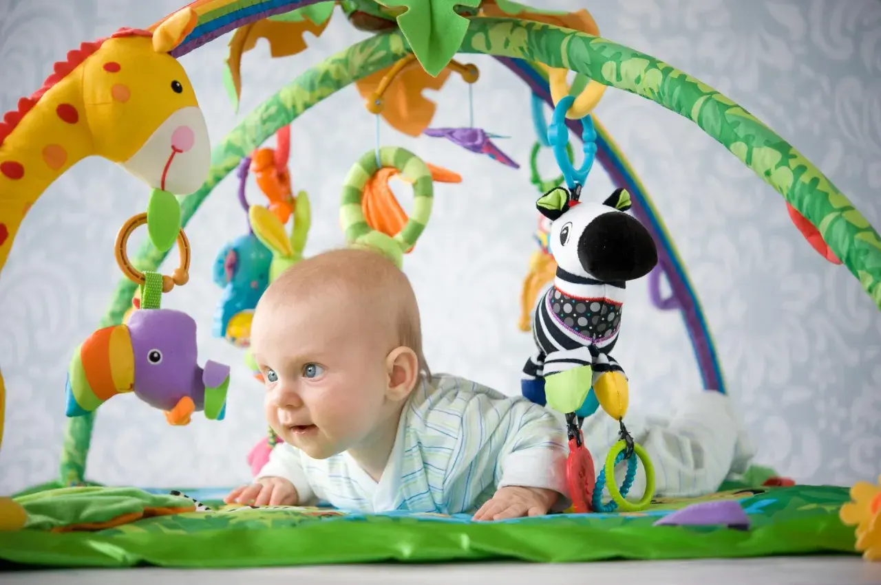 Niemowlę leży na macie edukacyjnej z zabawkami: żyrafą, zebrą i ptaszkiem.