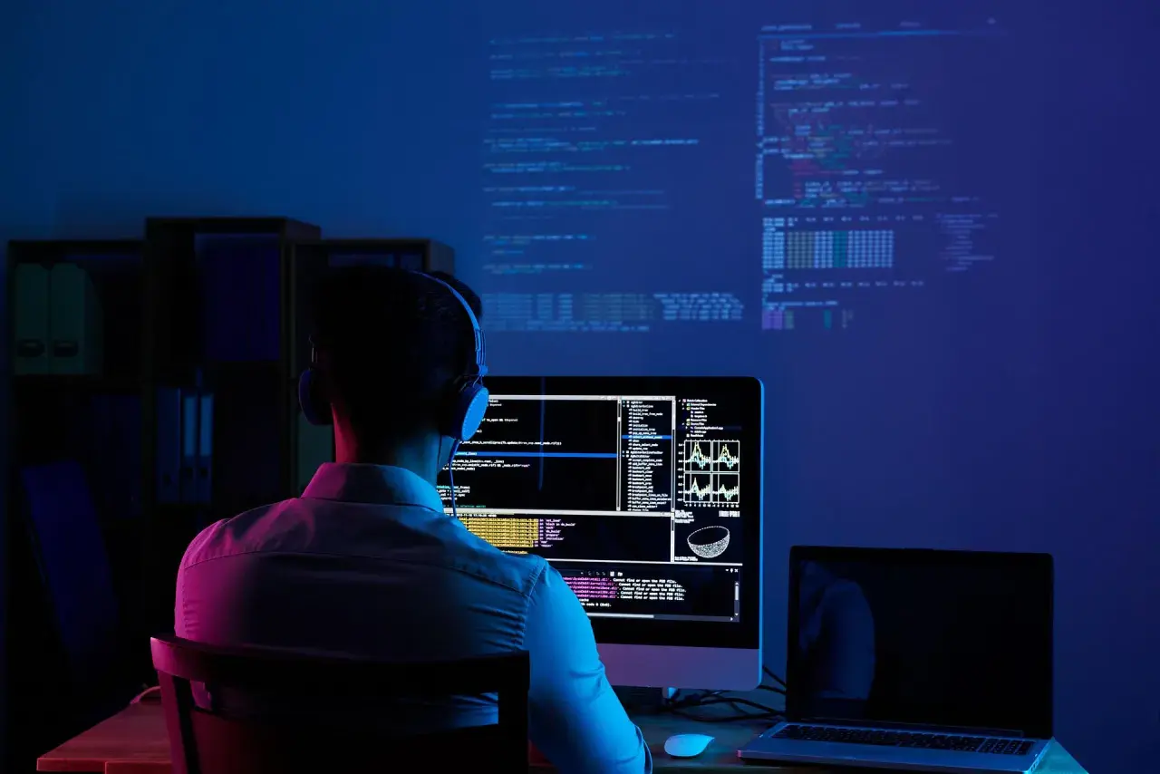 Młody człowiek w słuchawkach pochłonięty kodowaniem na ekranie. To idealne miejsce do nauki cyberbezpieczeństwo studia.