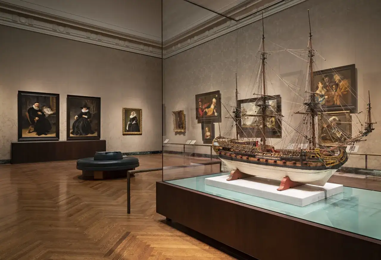 Model żaglowca i obrazy w muzeum. Wystawa prezentuje bogactwo historii sztuki, od portretów po morskie opowieści.