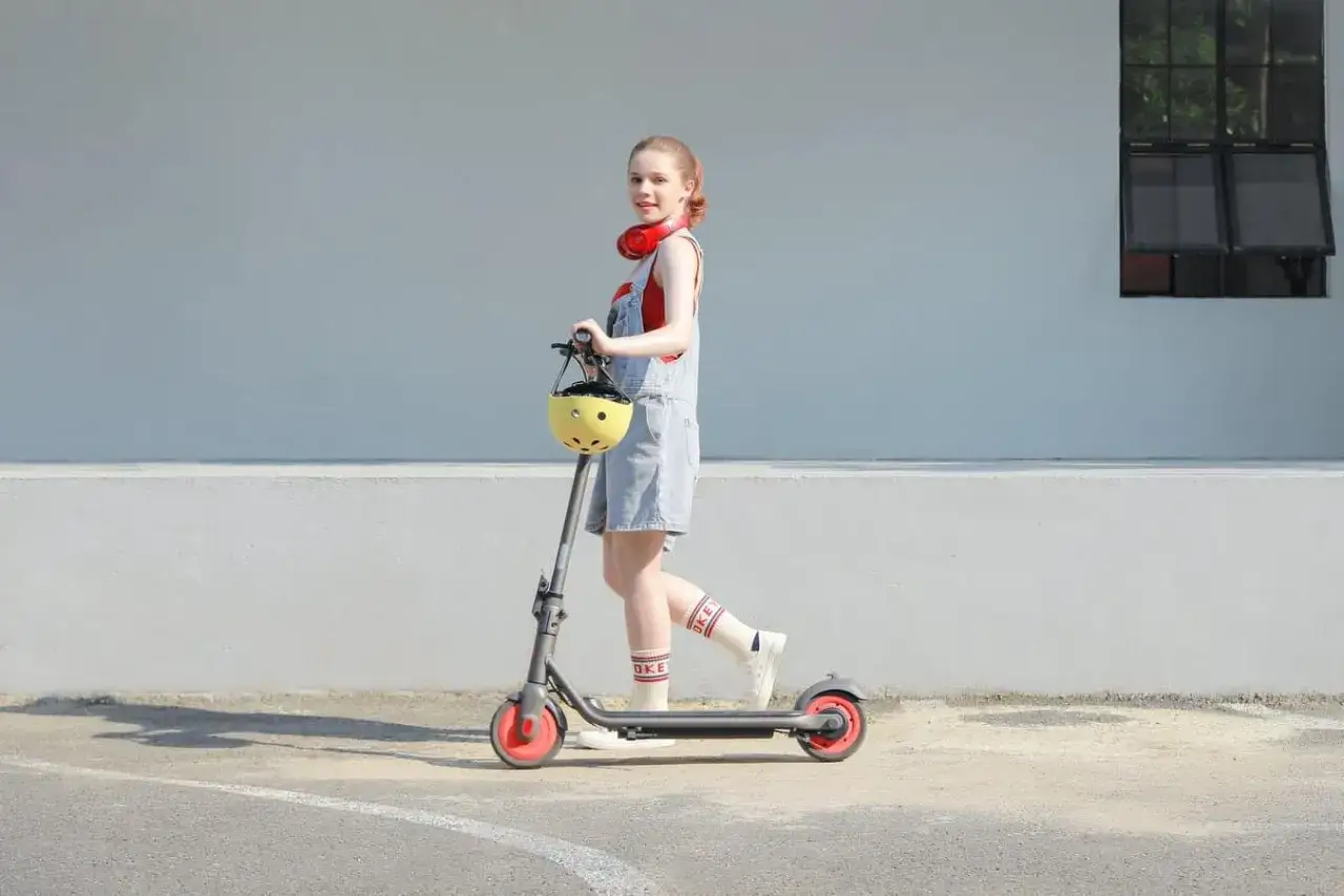 Dziewczynka z kaskiem na hulajnodze elektrycznej. Od ilu lat można jeździć na hulajnodze elektrycznej? To pytanie nurtuje wielu młodych miłośników tego pojazdu.